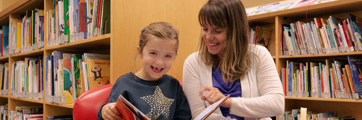 A woman and a girl reading a book at the library