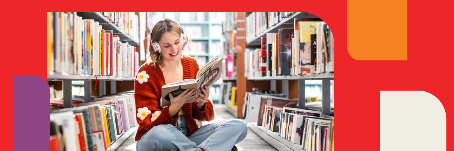 Young adult sitting in between shelves of library books, reading a book and listening to music