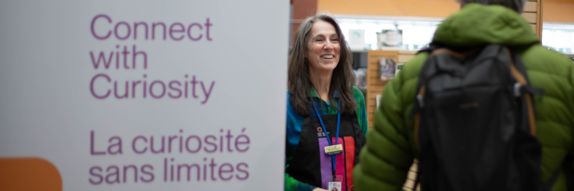 Librarian standing beside a rollup banner with the OPL tagline "Connection with Curiosity"